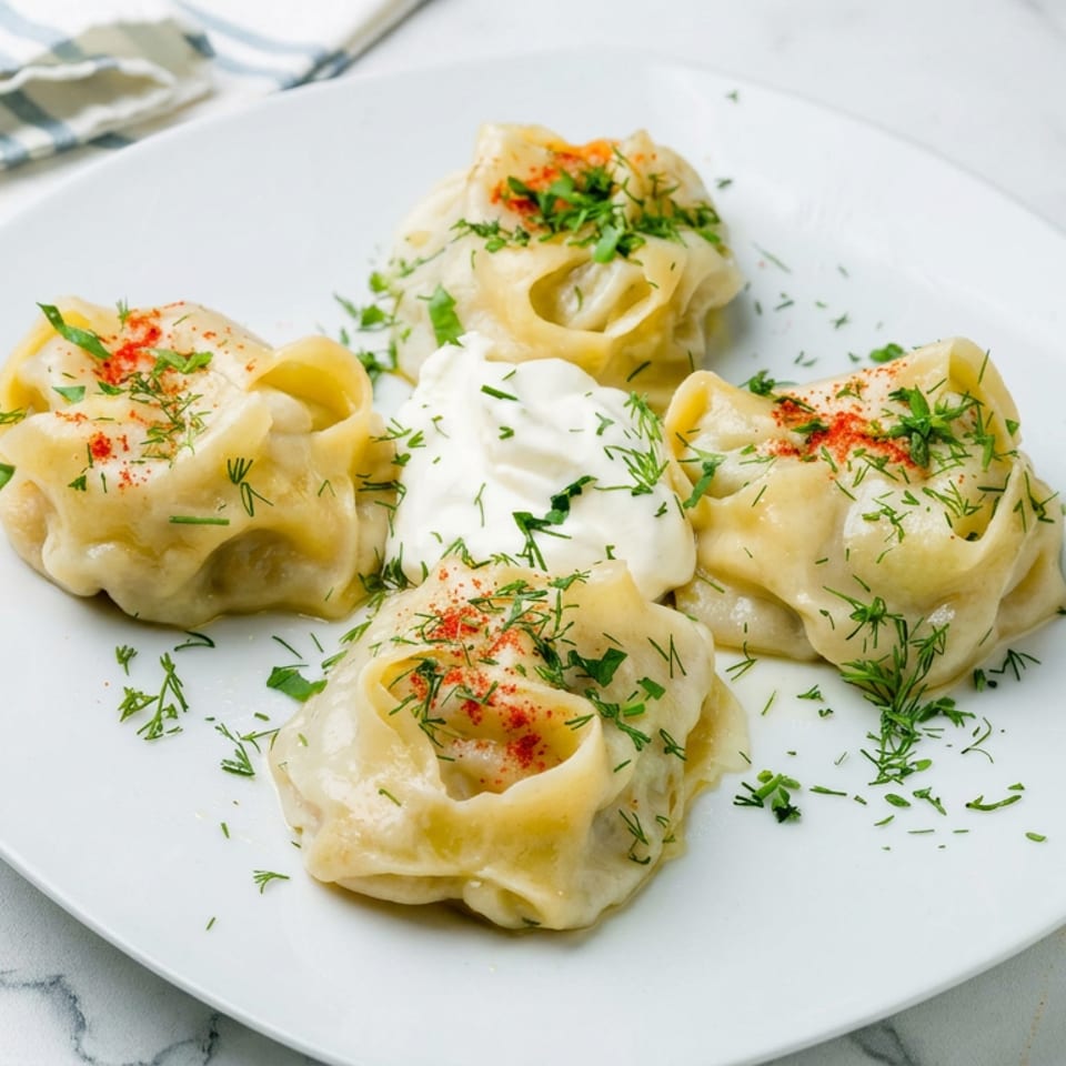 Four dumplings topped with sour cream, fresh dill, parsley, and paprika on a white plate.