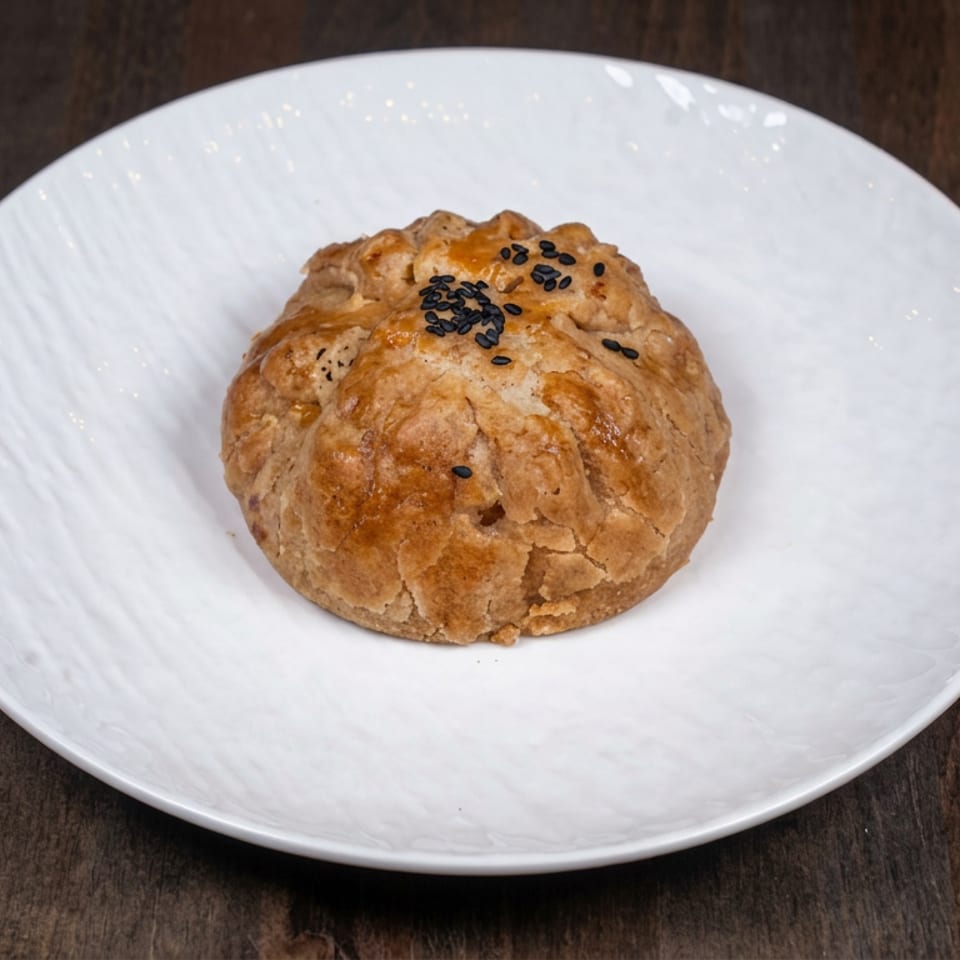 Golden-brown, sesame-topped pastry served on a white plate atop a dark wooden table.