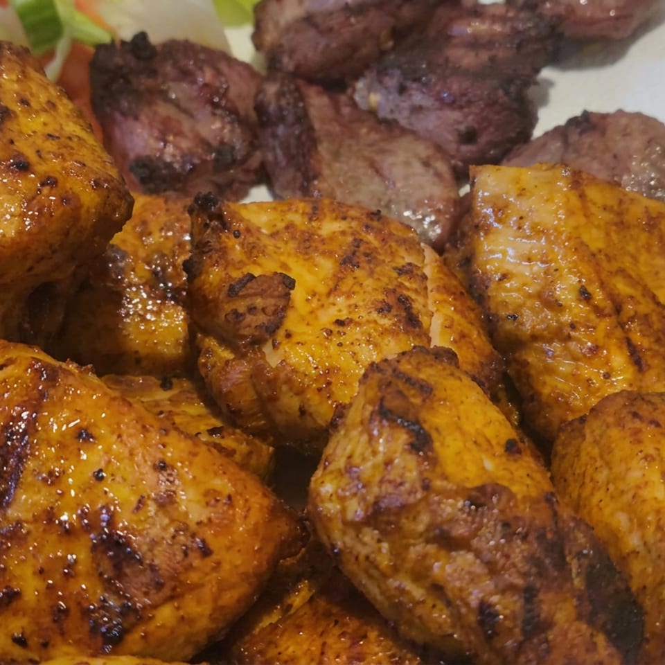 Platter of golden grilled chicken pieces and browned meat, garnished with vegetables on a white plate.