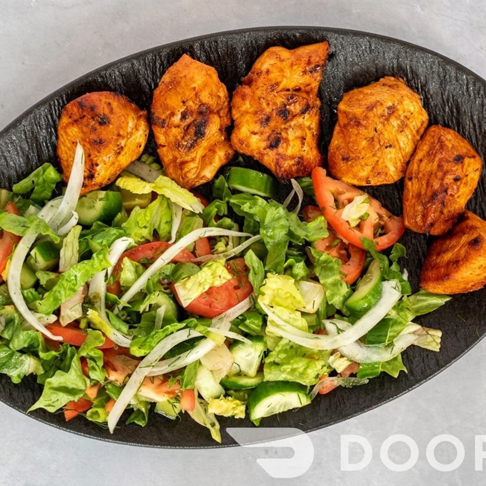 Black platter of grilled orange chicken pieces served with a fresh lettuce, tomato, cucumber, pepper, and onion salad.