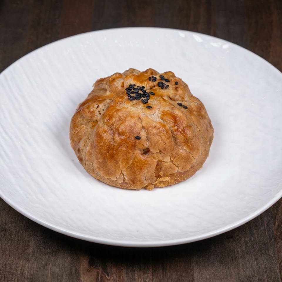 Golden-brown sesame-topped pastry served on a white plate atop a dark wooden table.