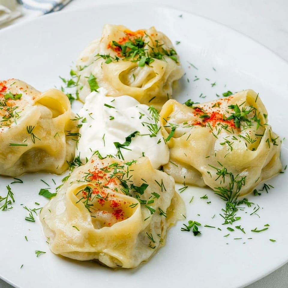 Four steamed dumplings topped with sour cream, dill, parsley, and paprika on a white plate.